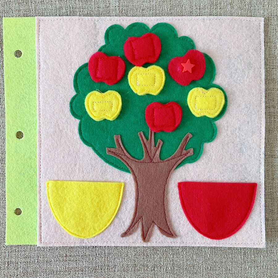 a page of the quiet book showing a green tree with yellow anbd red fruit hanging two pockets to store the fruit shapes when not attached to the tree