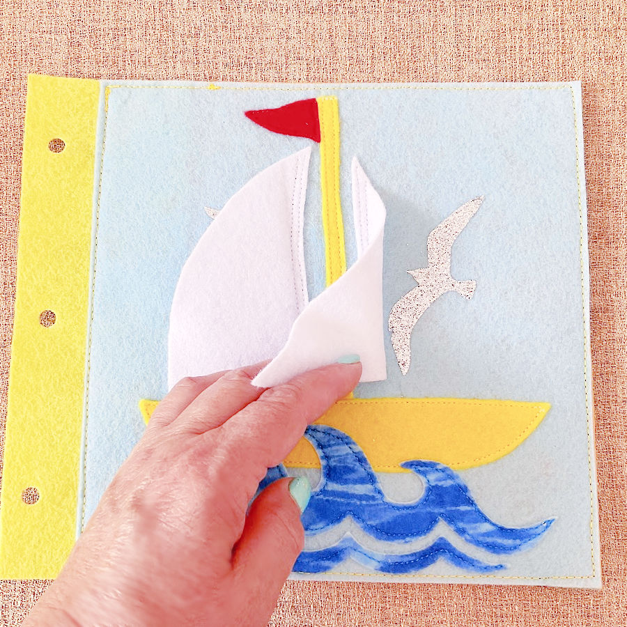 a page fro the quiet book showing a sailboat a womans hand lifts the sail to show a bird