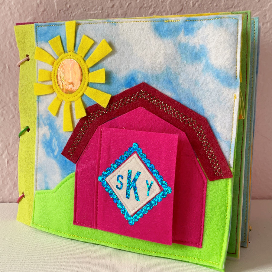 page 1 of the quiet book showing the sun, house and the barn door which opens to a pocket containing the image of the owner