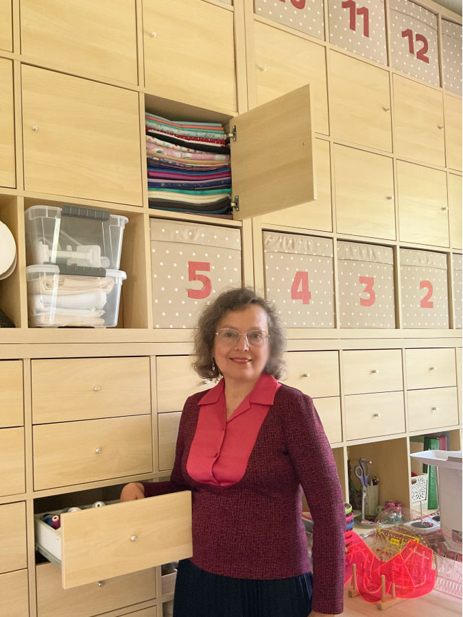 a woman in front of a storage system made with Ikea Kallax units showing storage for fabric and also drawers for thread and other sewing notions