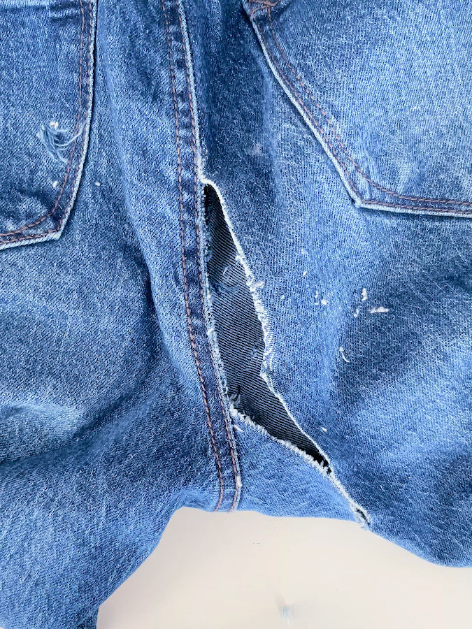 the rip in the jeans after the loose threads were trimmed in preparation for mending