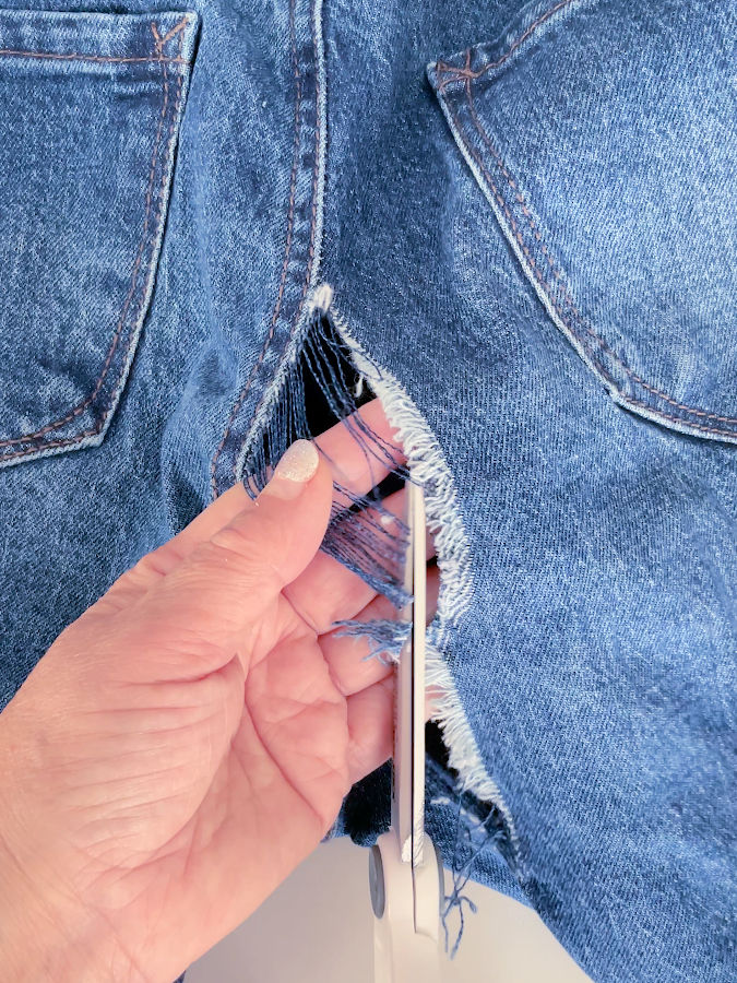 trimming the hole in the jeans before starting the mending a womans hand holds some loose threads while a pair of scissors cuts them