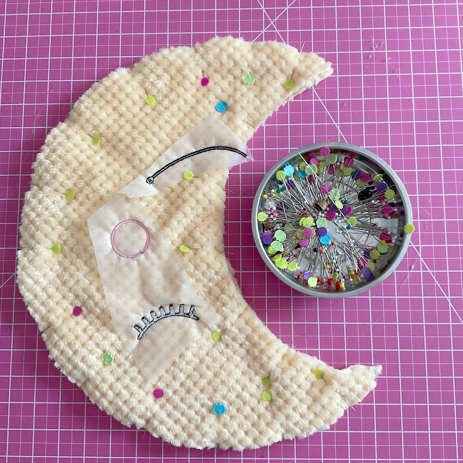 the moon plushie after embroidery and pinning of the two sides the embroidery stabilizer pieces are still visible on the fabric