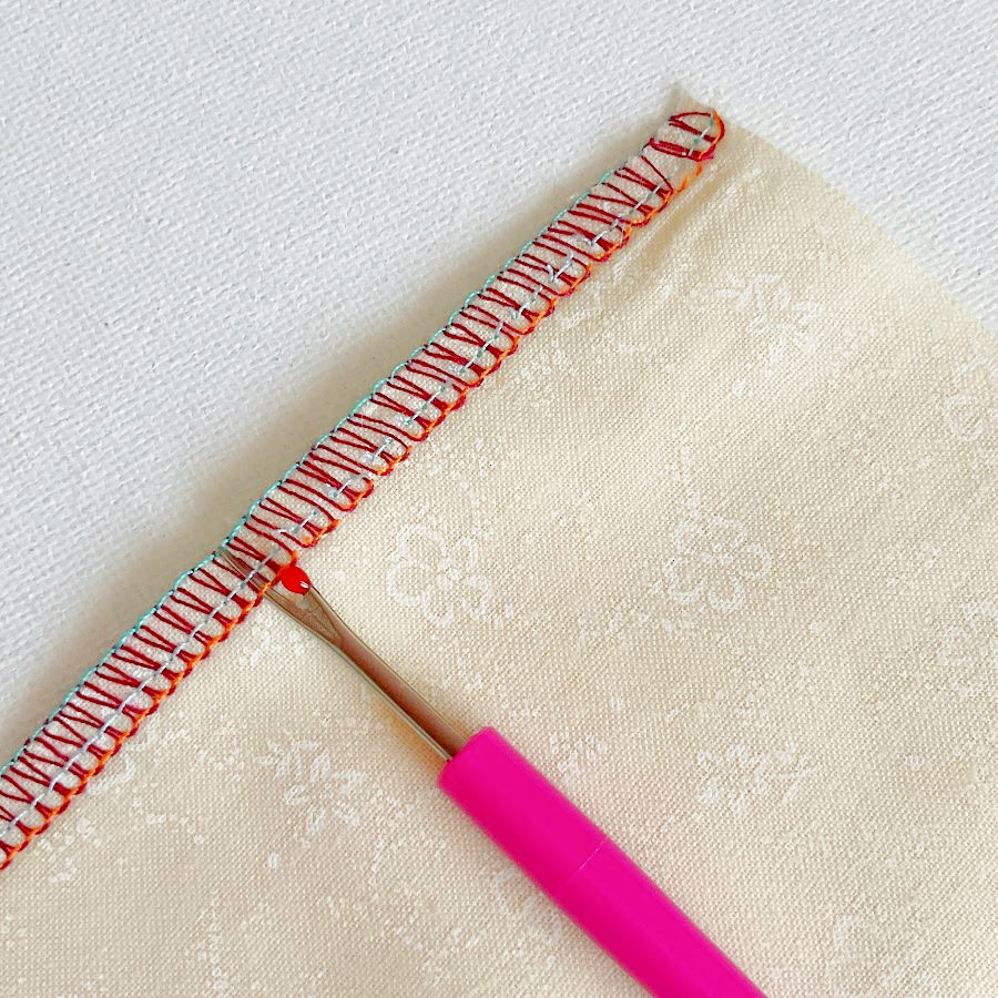 a seam ripper being used to snip the two needle threads in a serger overlock seam in order to prepare for removing the thtreads of the seam completely