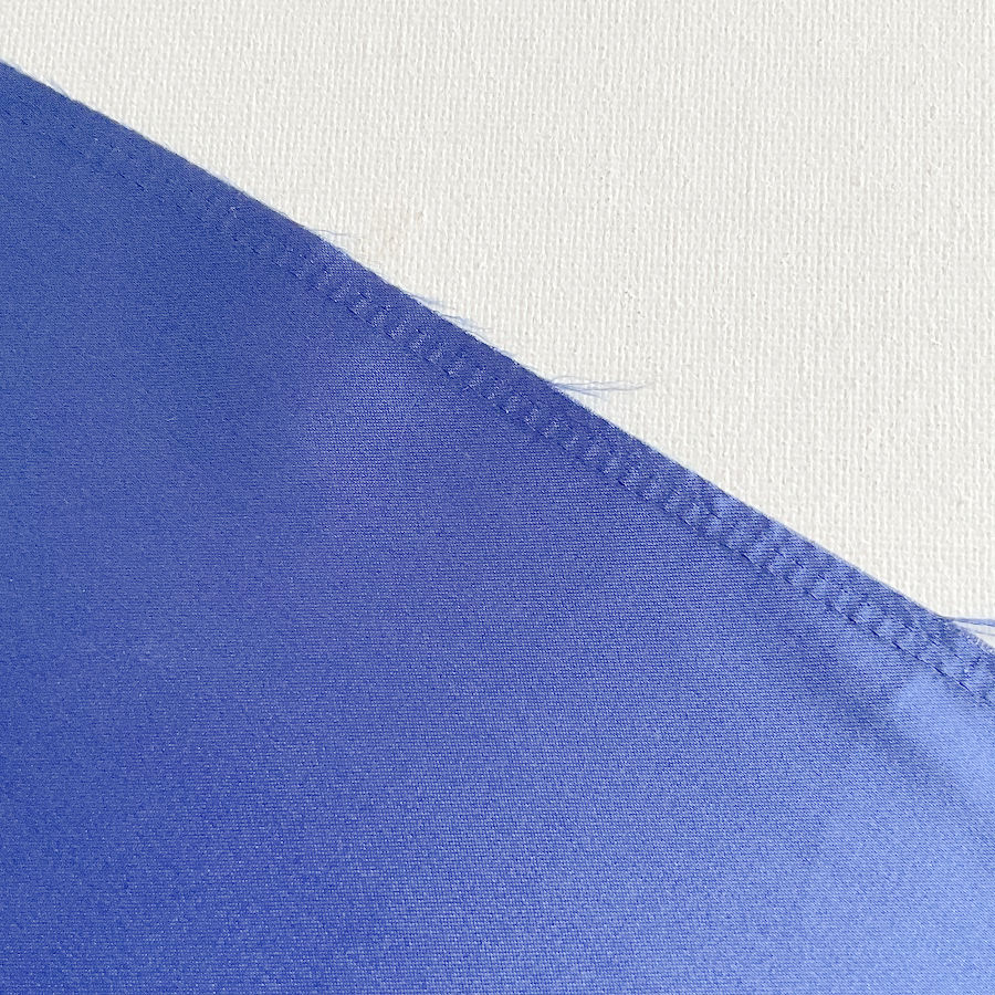 a piece of fabric after the serger overlock stitch was removed it shows some fraying and the place of the old seam is clearly visible