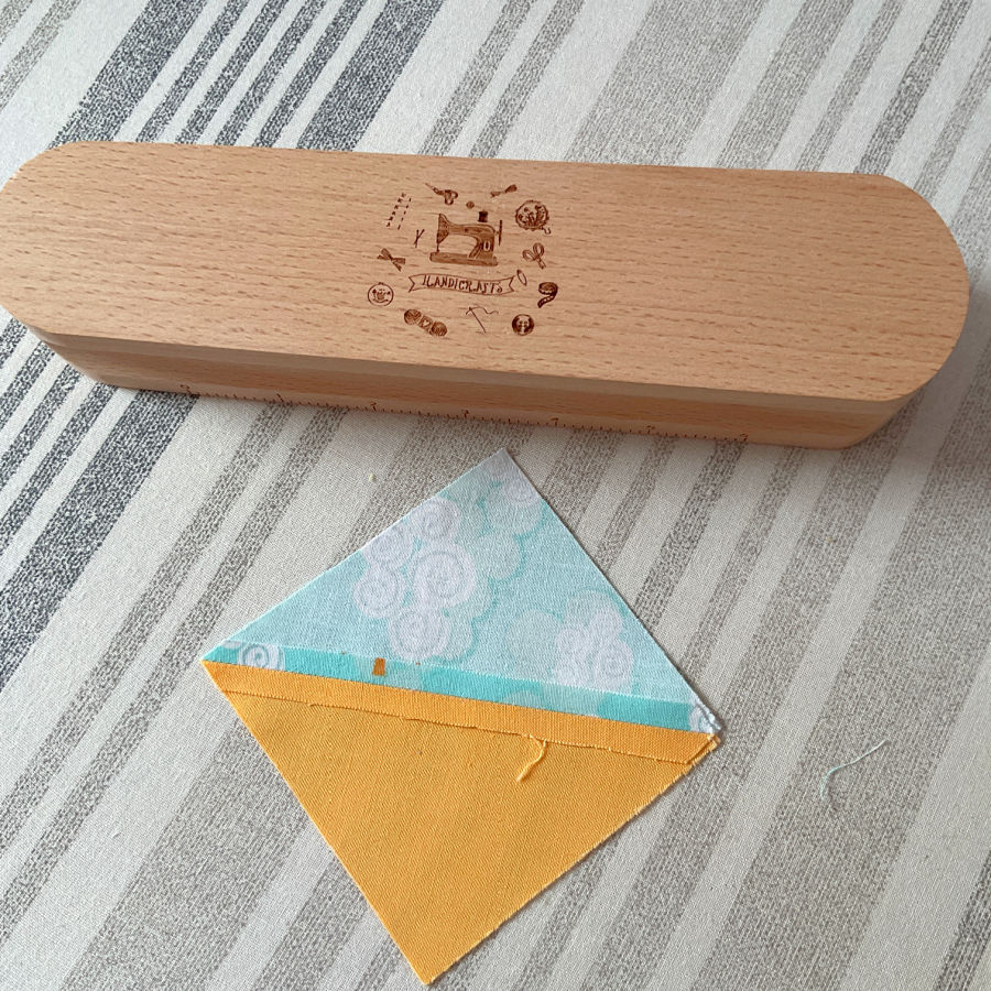 a wooden clapper and a half square triangle on an ironing table the seam pressed with the clapper looks perfect