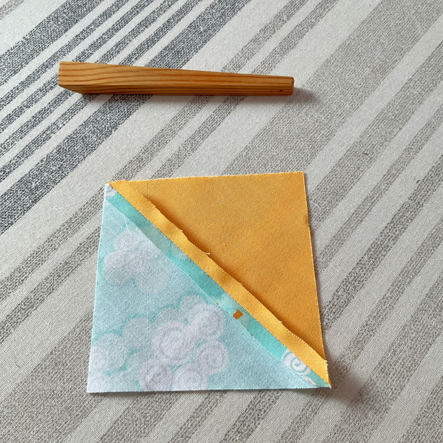 a wooden finger presser and a half square triangle after pressing the pressed seam is not perfect