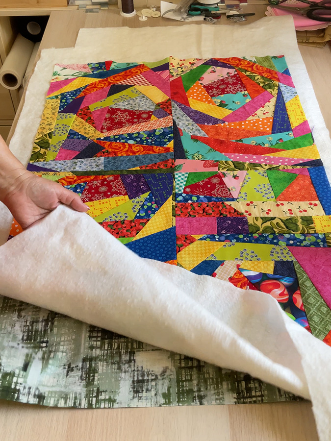 the quilt sandwich presented on a cutting table the top crumb panels, the backing and the bating are visible