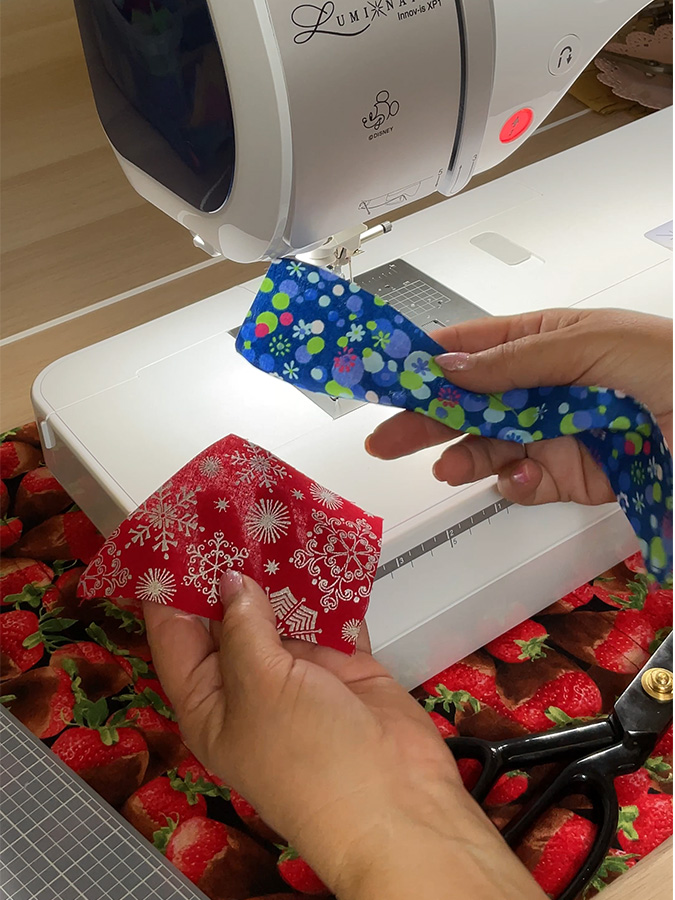 a woman holds the first two crumb pieces of fabric that will be joined a sewing machine in the background