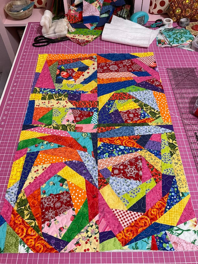 quilted pieces of fabric made out of crumb bits of fabric sitting on a cutting table more leftover fabric in the background