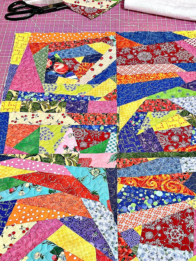 four crumb blocks quilted together displayed on a sewing table a pair of tailors scissors in the background