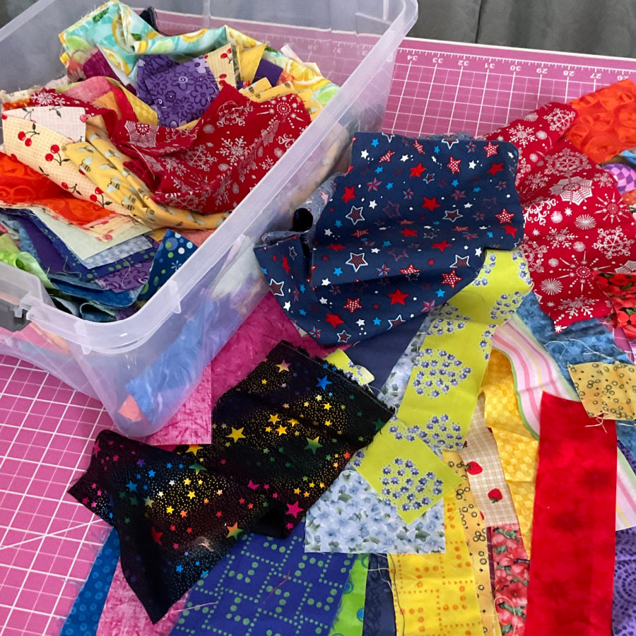 small pieces of fabric crumb fabric pieces in a pile on a sewing table and another pile in a storage container on the same table