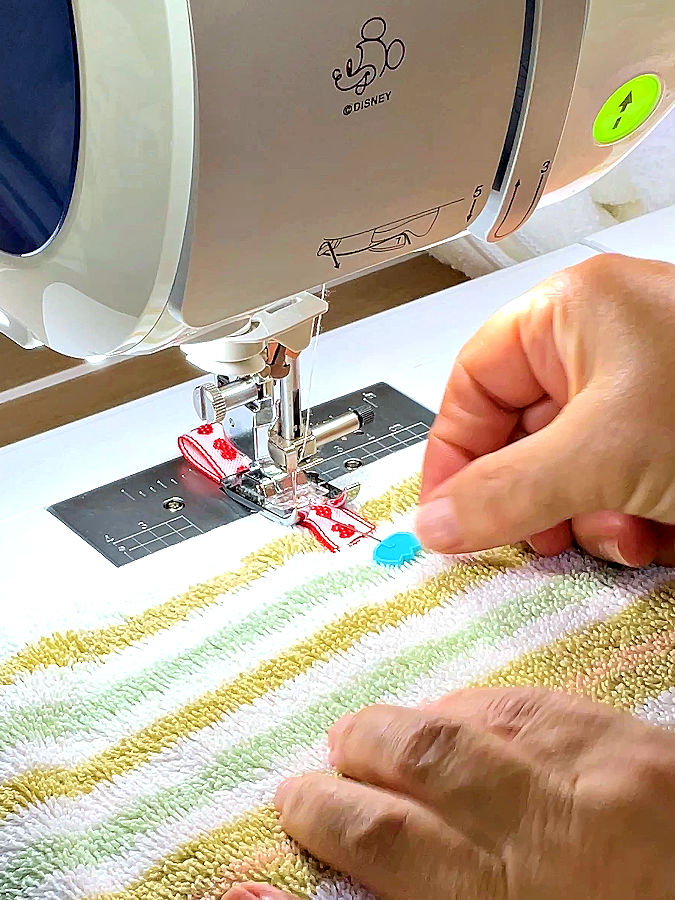sewing machine needle assembly while sewing the ribbon loop to the towel a pin still visible in the ribbon