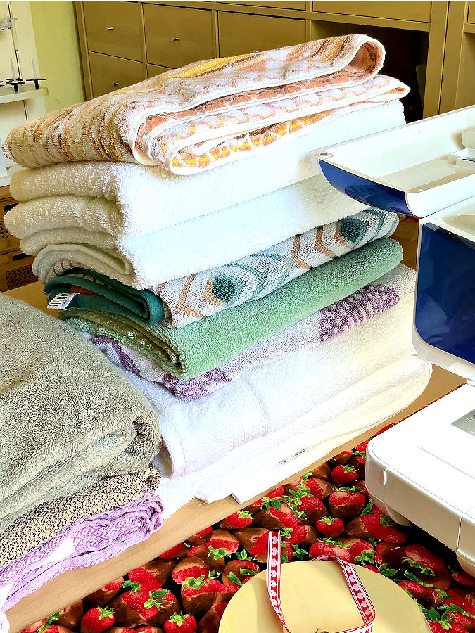 a stack of towels and a loop of ribbon on a table near a sewing machine from which only a small corner is visible