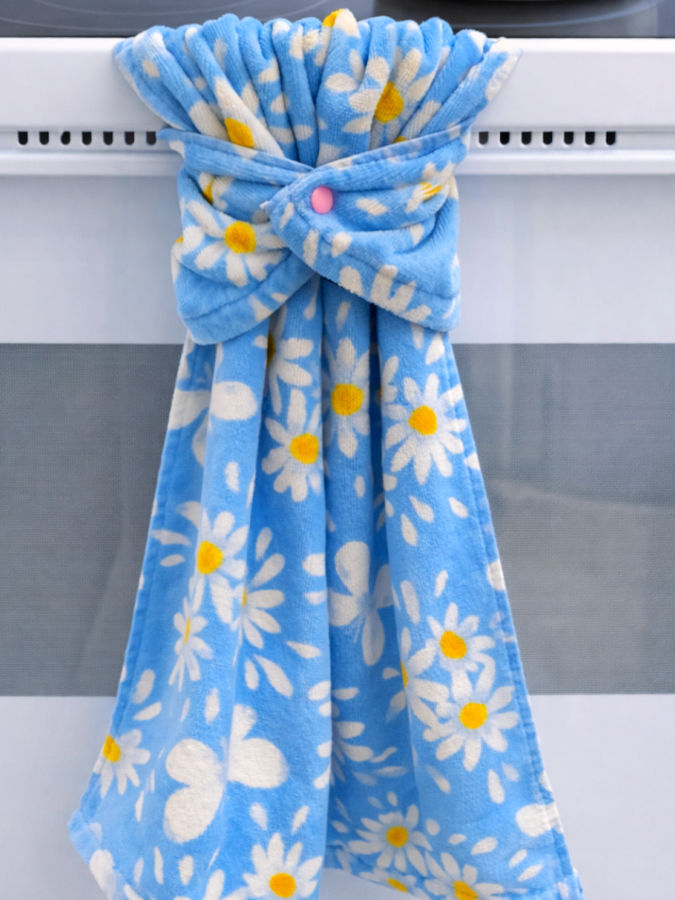 a blue towel with a daisy motif using a plastic snap shown hanging on the handlebar of a white stove