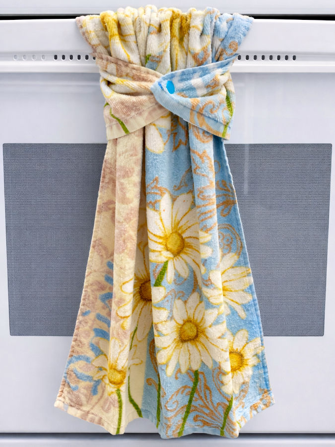 a multi colored kitchen towel using a plastic snap shown hanging on the handlebar of a white stove