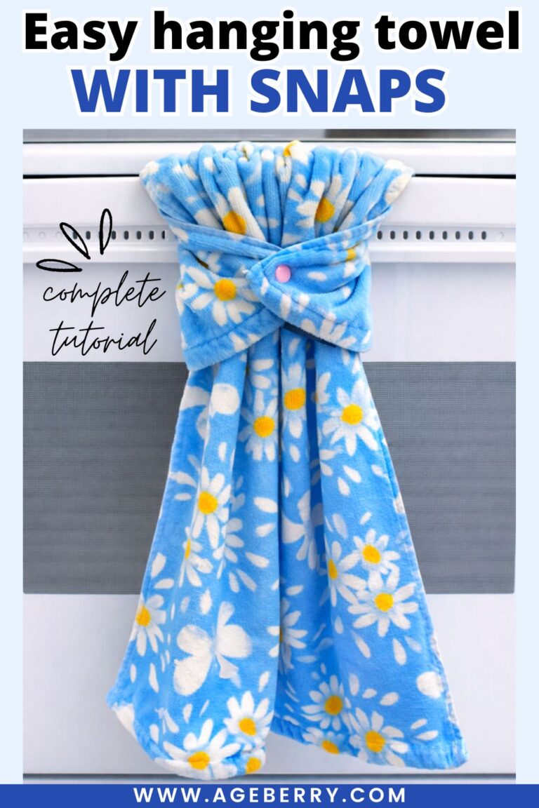 Blue floral kitchen towel hanging from a stove handle using a plastic snap closure. The towel is wrapped around the stove rod and fastened at the front with a pink snap, creating a secure hanging towel without sewing. The image shows how snaps can replace traditional hanging towel holders