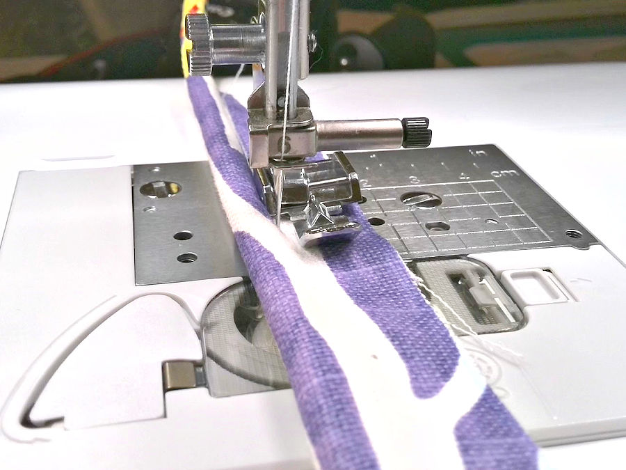 sewing machine needle assembly with a zipper foot installed shown while sewing the corn into the piping