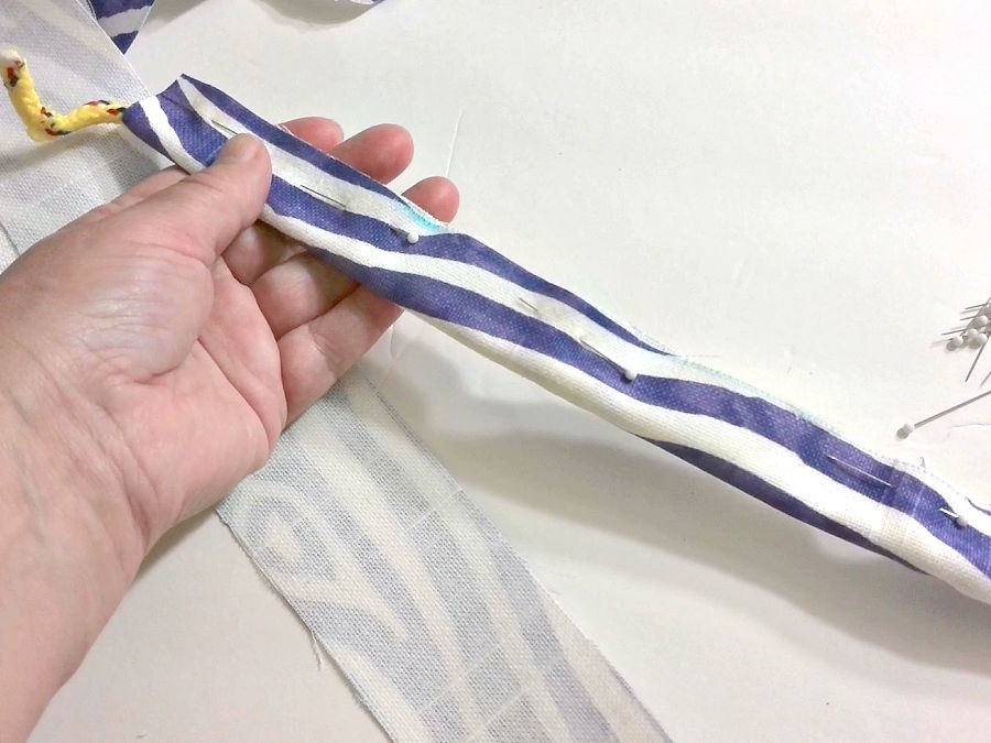 folding the fabric over the cord and using pins to hold the assembly together before sewing