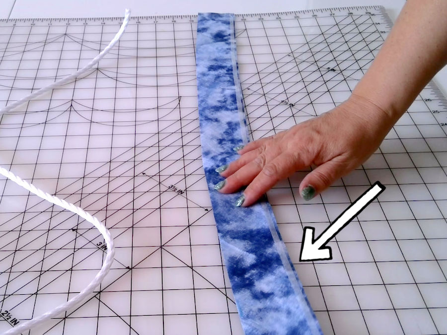 using wonder tape a womans hand shown pressing a strip of wonder tape to the edge of the fabric strip after removal of the protective paper from the tape the cord to be wrapped near the strip