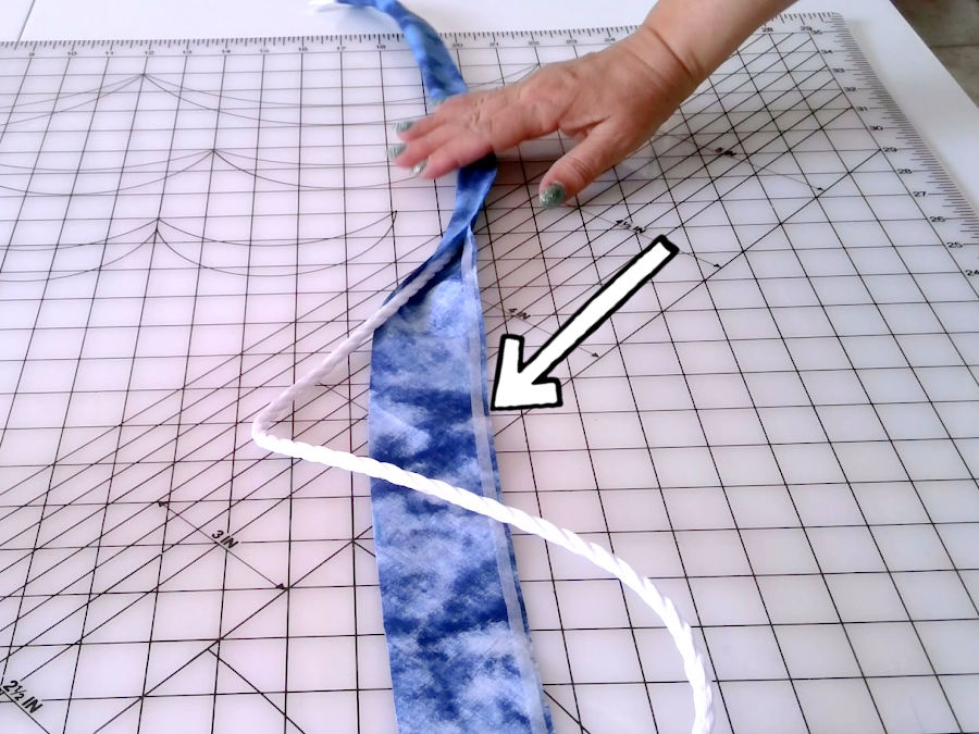 a womans hand shown while folding the fabric strip over the cord for piping and pressing the wonder tape strip to secure the assembly