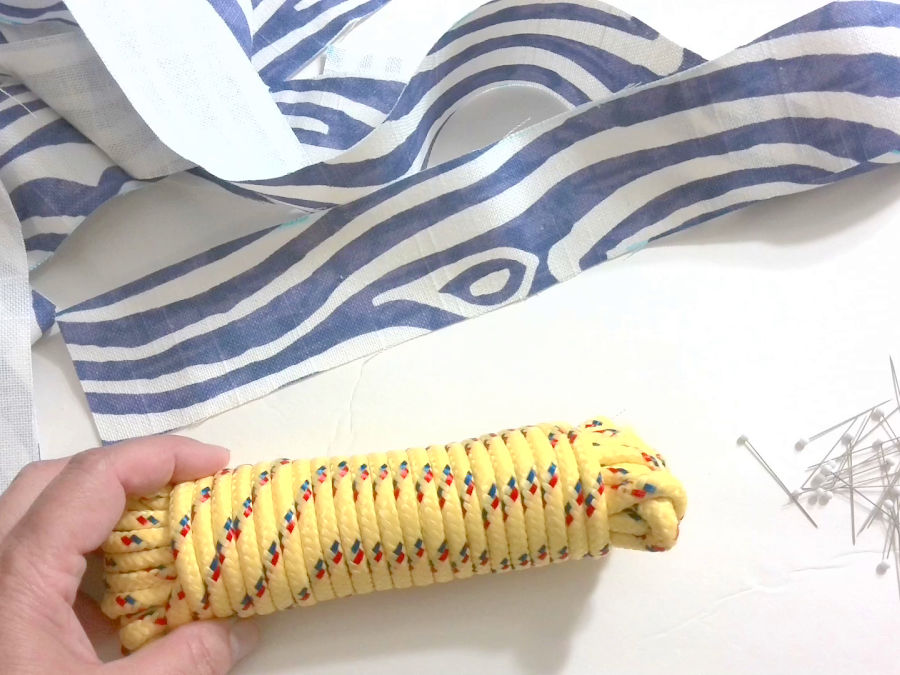 image shows a length of cord tightly wrapped in a number of sewing pins and a piece of material cut in preparation for making piping