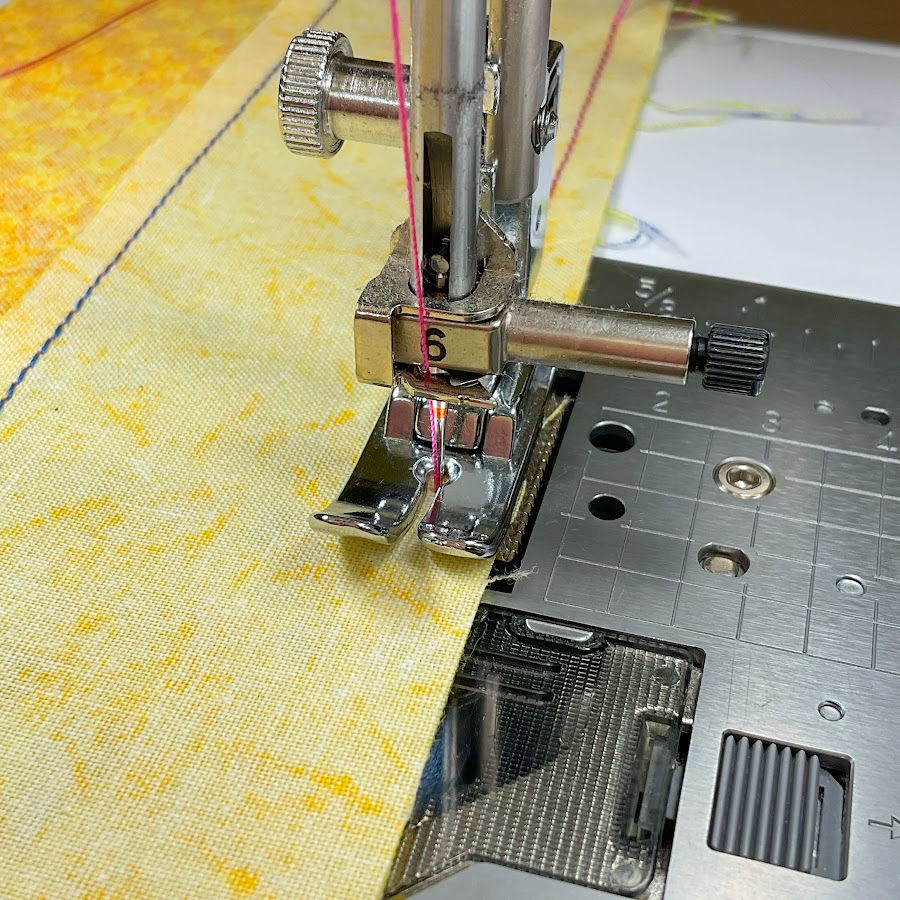 true quarter inch presser foot with no guide shown installed on a sewing machine needle assembly