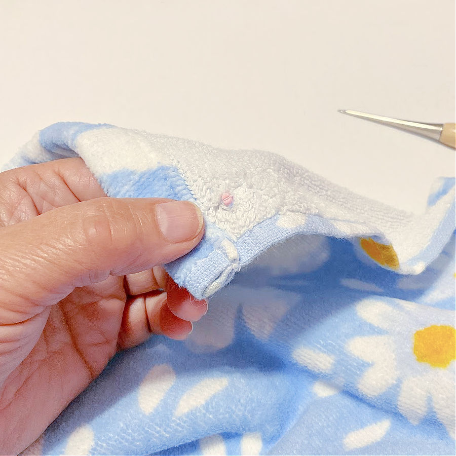 the cap part of the snap inserted in the hole in the towel the tip of the awl visible in the image