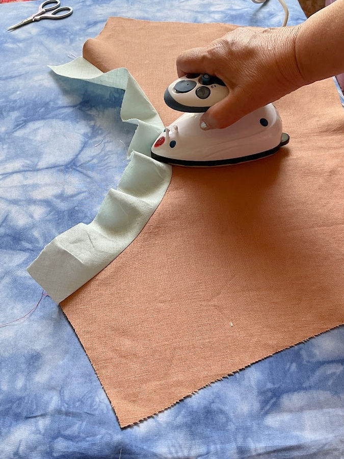 a womans hand using a mini iron to iron a the seam