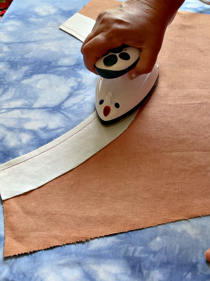 a womans hand shown when using a mini iron to press flat the seam after stitching