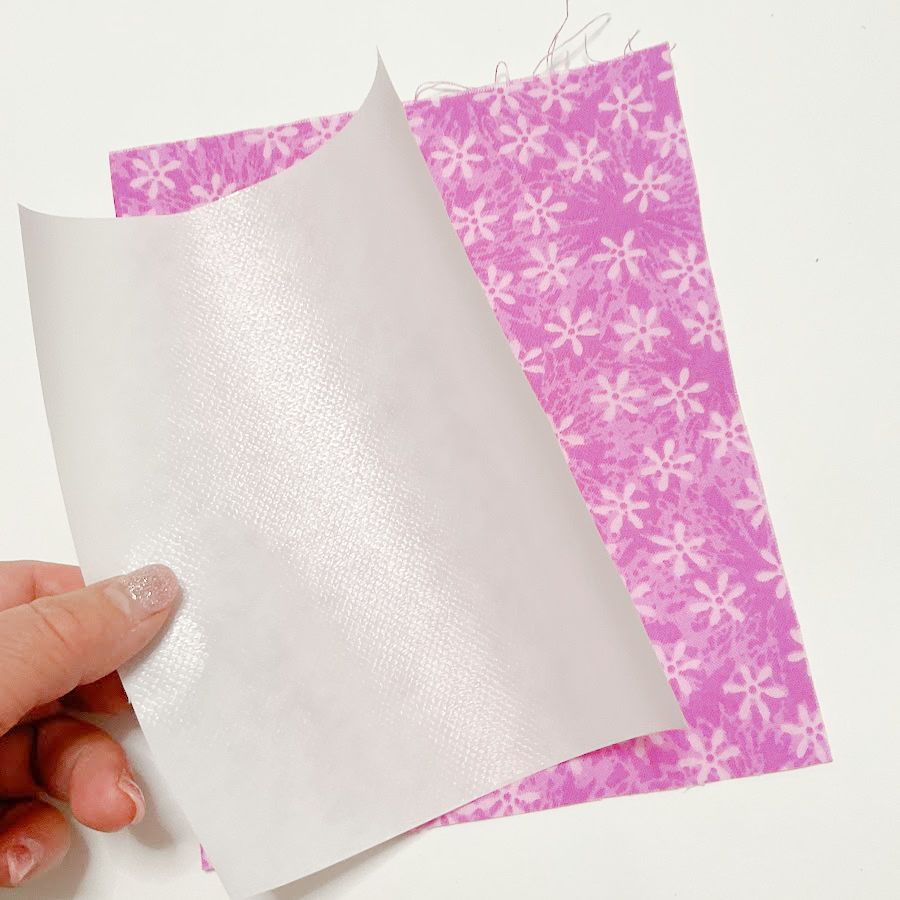 a womans hand holding a rectangle of heat and bond fusible interfacing slightly smaller than the fabric rectangle on which it is laid