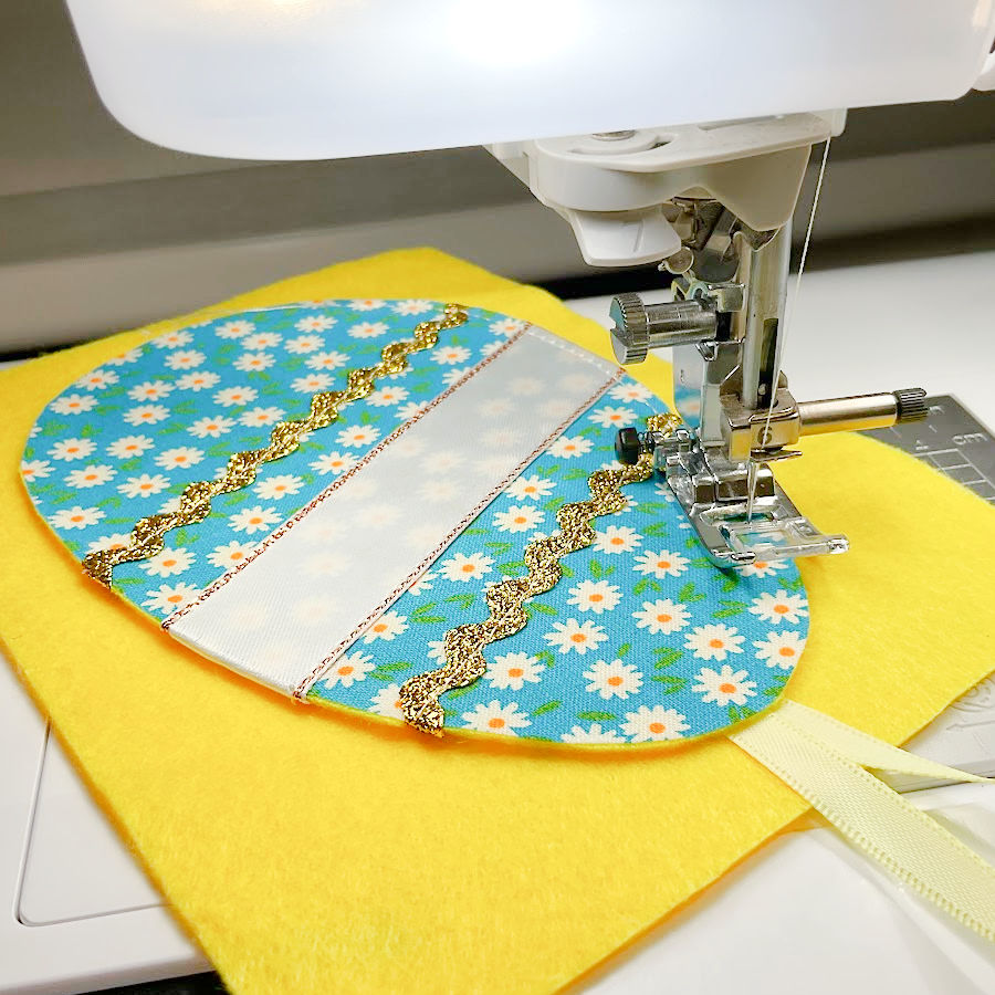 a sewing machine needle assembly shown while sewing the face of the egg to the piece of felt that will be its back the hanging loop is visible