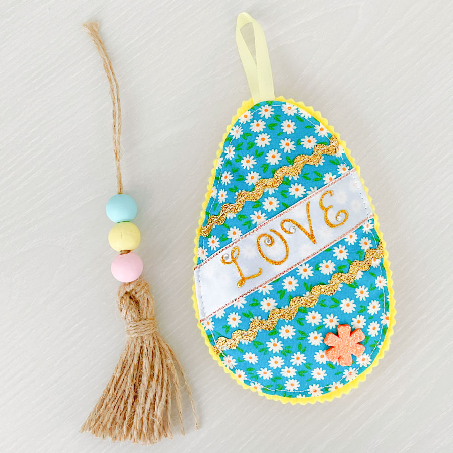 a single finished fabric easter egg with the word love on it paired with a tassel made out of jute fiber and a couple of beads