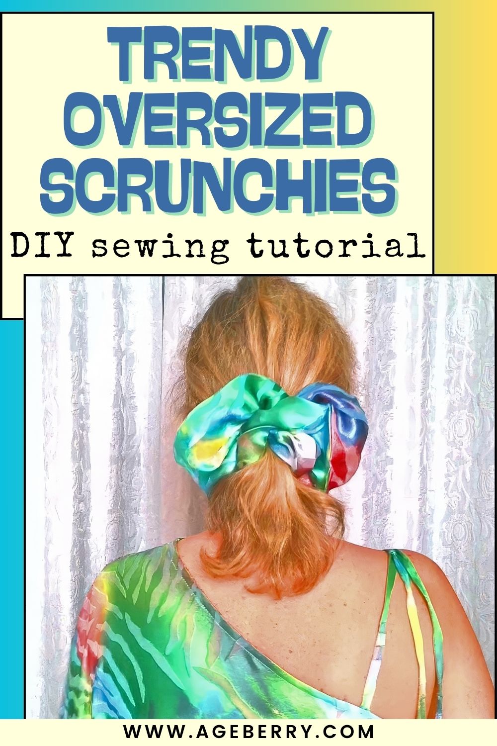A woman is shown from behind wearing a large, oversized satin scrunchie in a low ponytail. The scrunchie features bright blended colors including green, blue, pink, and yellow with a glossy sheen. She has shoulder-length blonde hair and is wearing a green patterned top with thin straps. The background consists of light-colored curtains, softly lit.