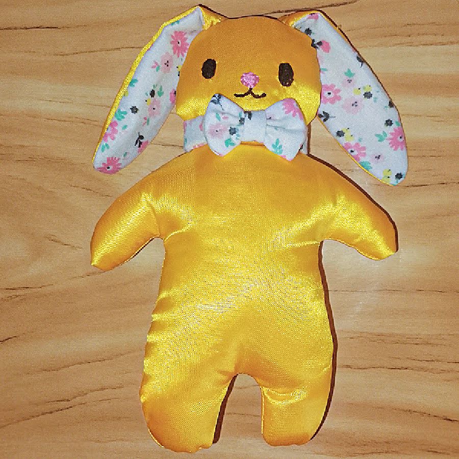 Finished stuffed bunny viewed from the front, with floppy floral ears, embroidered face, bow tie, and smooth, evenly stuffed body.