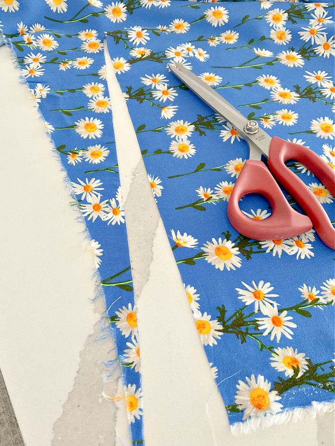 a piece of fabric in the process of being squared with the store cut edge clearly not perpendicular on the grainline a pair of scissors on the fabric