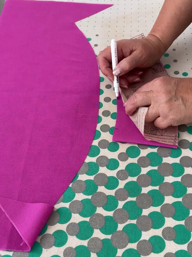 a womans hands shown while marking a piece of fused fabric from the corresponding piece of paper pattern