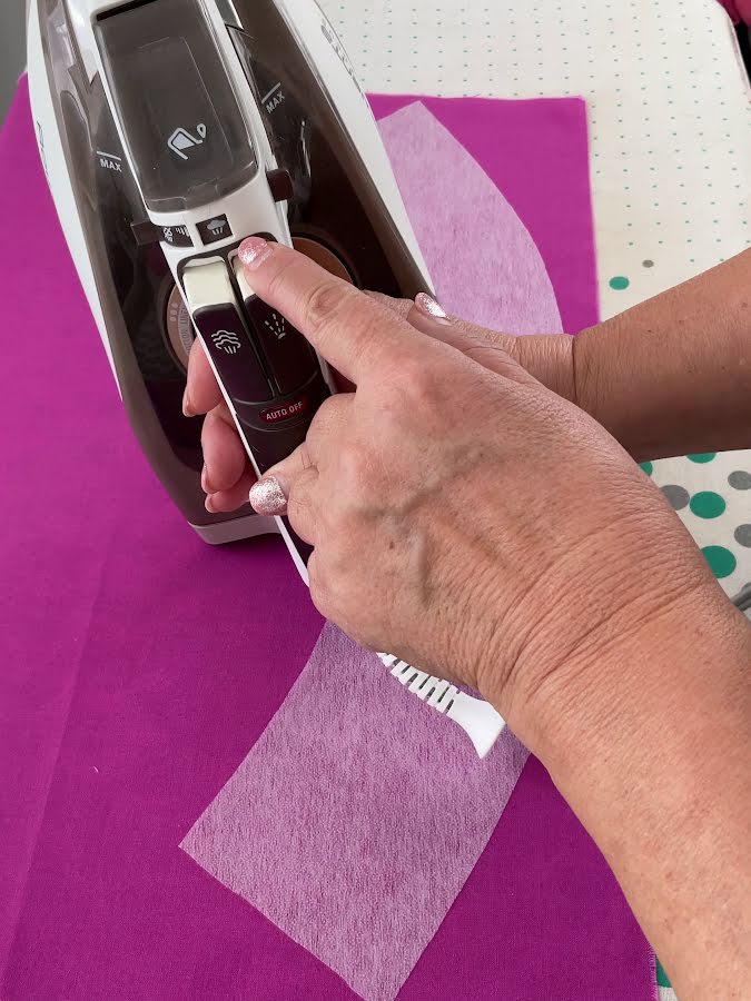 a woman pointing to the steam button on the iron