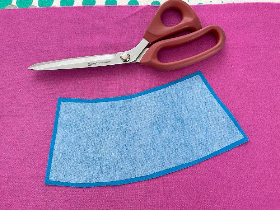 a piece of interfacing slightly smaller than the piece of material it is fused to a pair of scissors in the image also