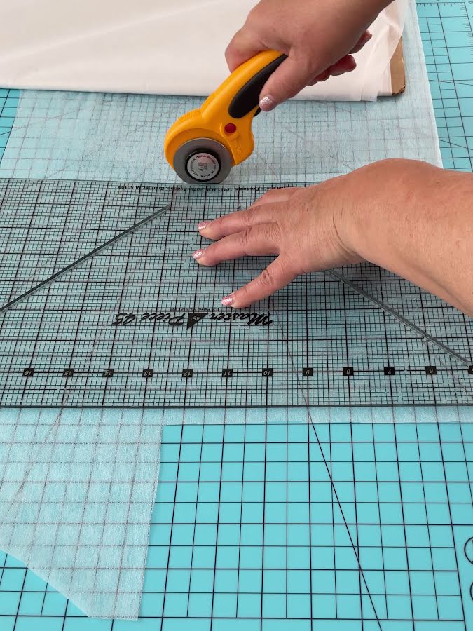 a woman cutting interfacing using a rotary cutter and a quilting ruler