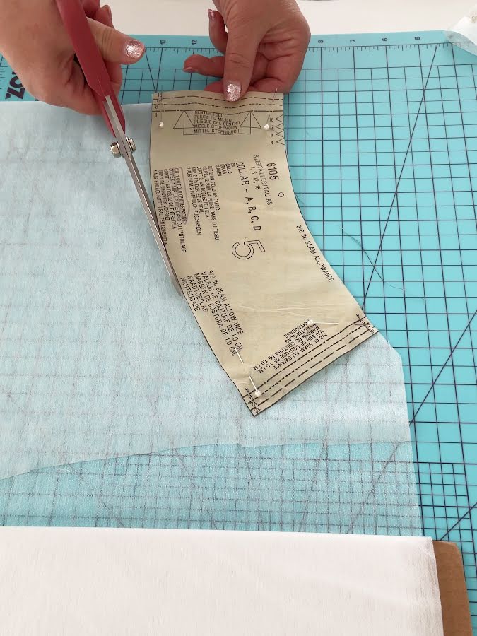 womans hands showing while cutting a piece of interfacing using a paper pattern