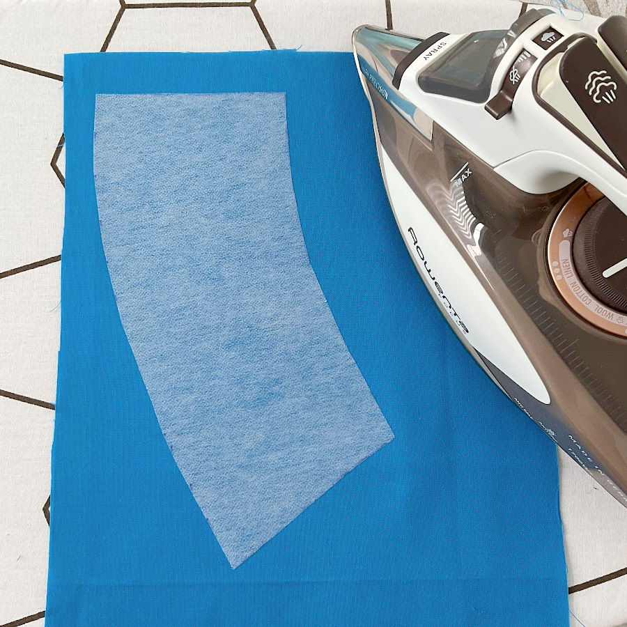 a piece of interfacing shown positioned on the fabric ready to be fused an iron visible in the image also