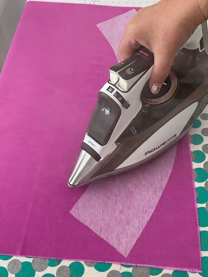 a womans hand using the iron to press down a small area of the interfacing to make it adhere to the fabric and prevent shifting while working with it