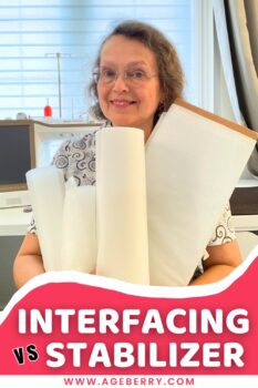 Woman in a sewing room holding several large rolls of white interfacing and stabilizer in her arms. A sewing machine and thread stand are visible in the background. The image features a red banner with white text reading “Interfacing vs Stabilizer” and the Ageberry.com website. The rolls vary in size and stiffness, showing different types of sewing support materials