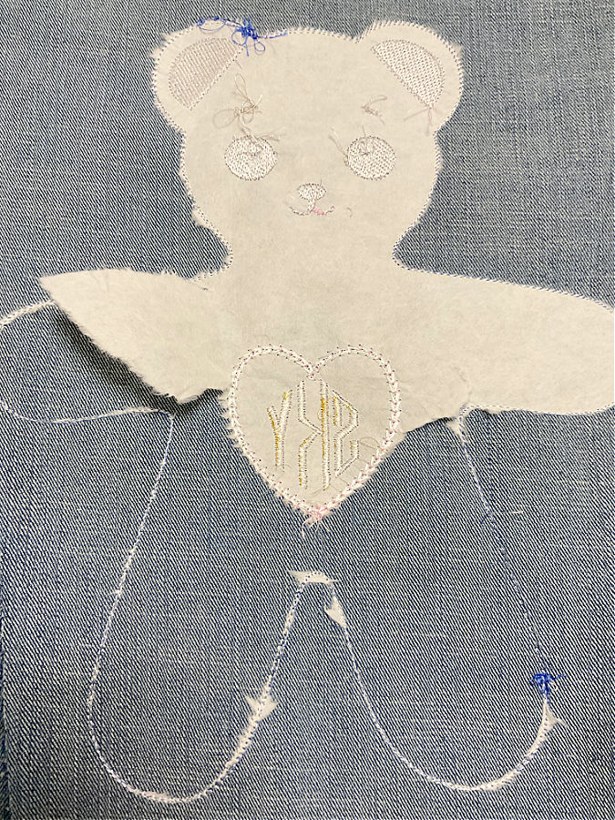 a finished embroidery design in the shape of a bear with stabilizer partly removed