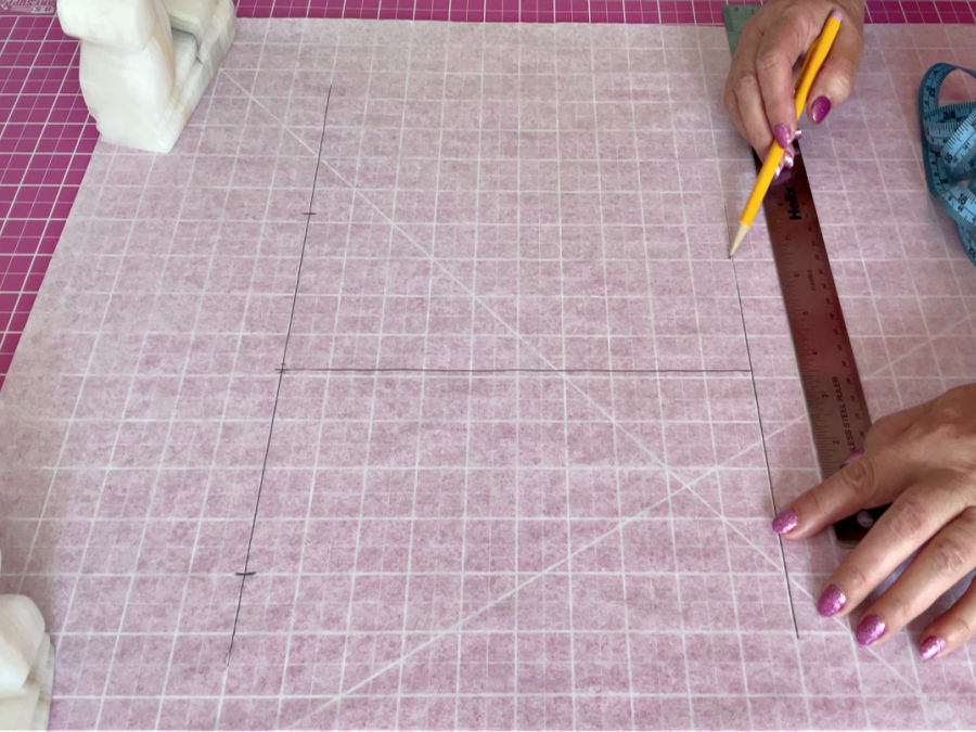 a sheet of tracing paper sitting on a cutting mat which has a grid of markings visible under the paper a woman drawing lines on the paper
