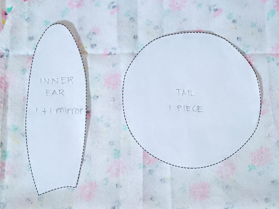 Inner ear pattern piece and circular tail pattern laid on fabric, labeled with cutting instructions including 1+1 mirror for ears and one piece for the tail.