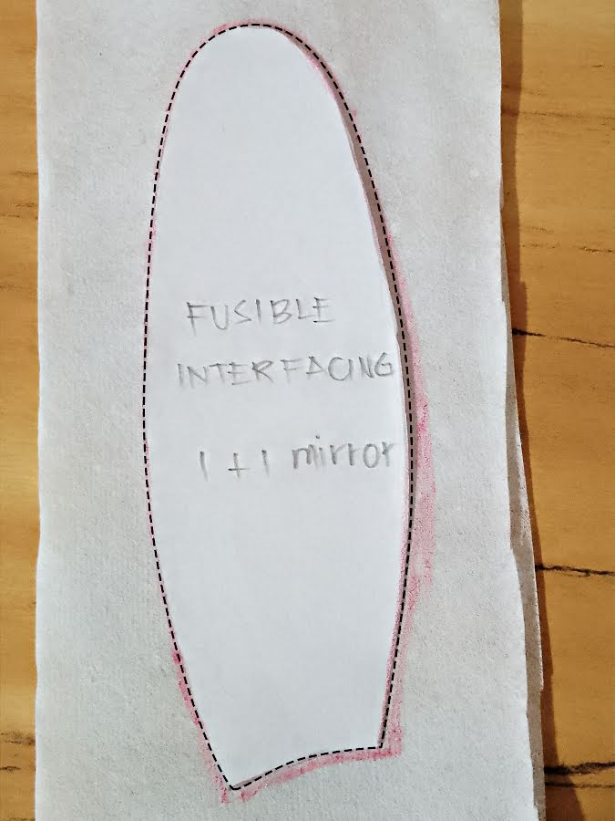Fusible interfacing pattern piece for a soft toy ear, traced on white interfacing with dashed cutting line and notes showing 1+1 mirror cutting.