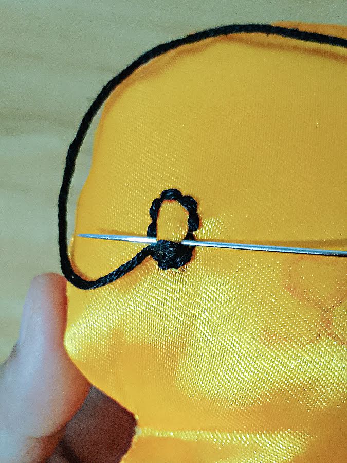 Close-up of soft toy eye being filled with satin stitch, showing black thread laid closely side by side inside the backstitched outline to gradually cover the fabric.