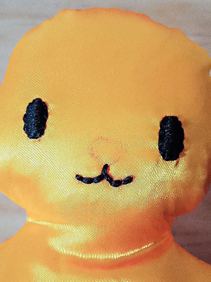 Soft toy face showing the mouth embroidered with short backstitches, forming a neat curved shape beneath the nose after both eyes are finished.